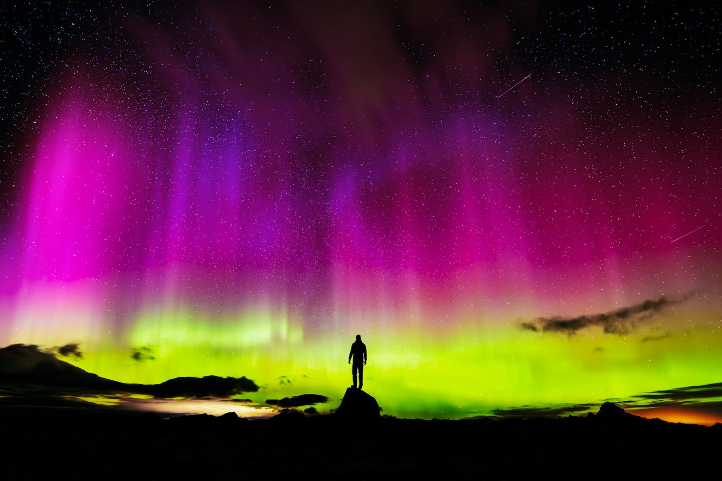 Figure silhouetted on rock watching the northern lights.