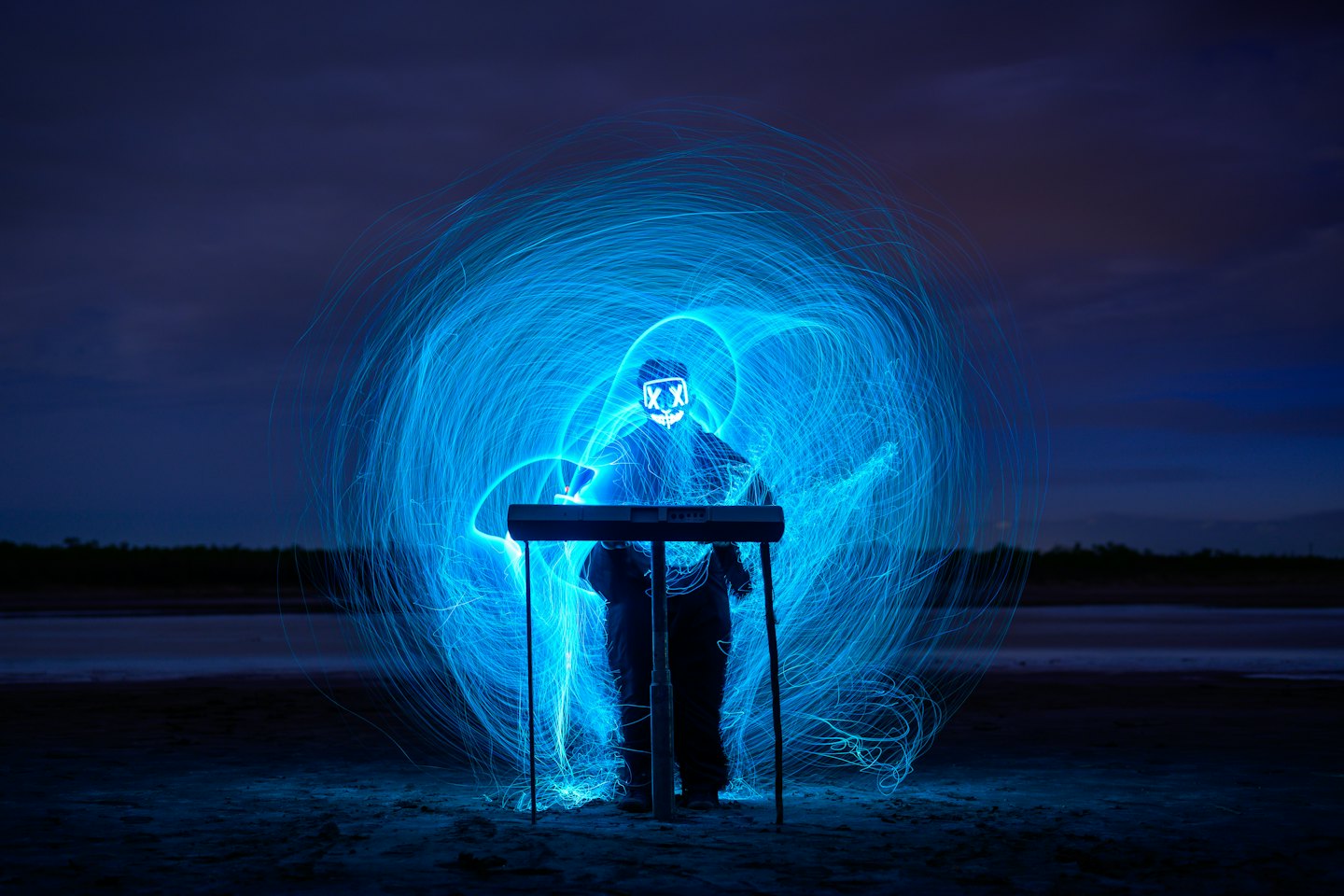 Person in a glowing mask plays a keyboard synthesizer outdoors.