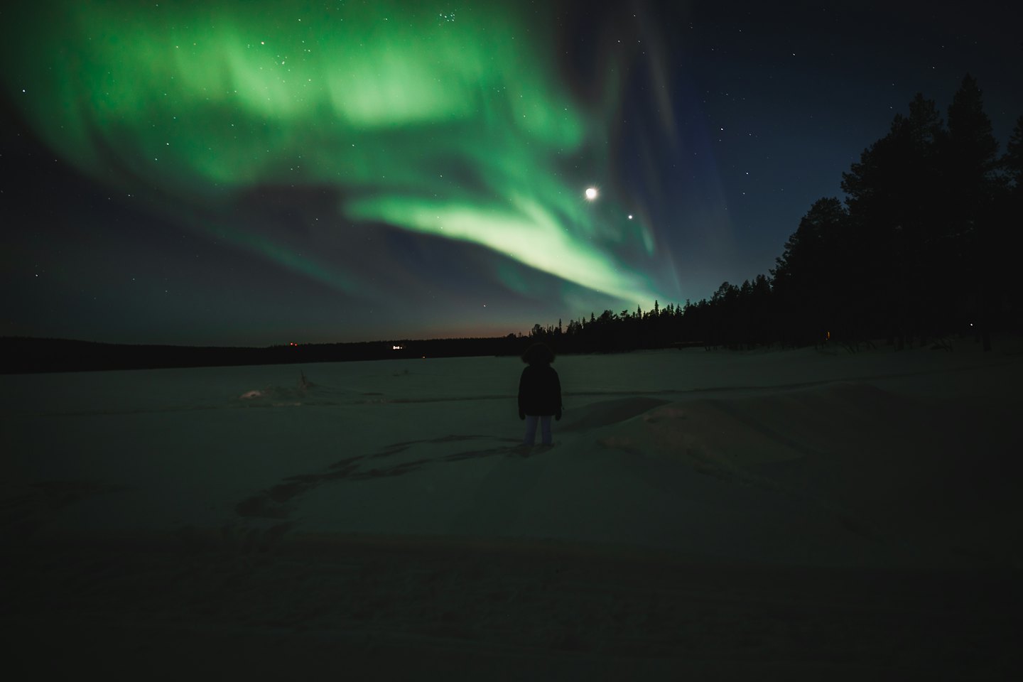 A person stands in the snow watching the aurora borealis.