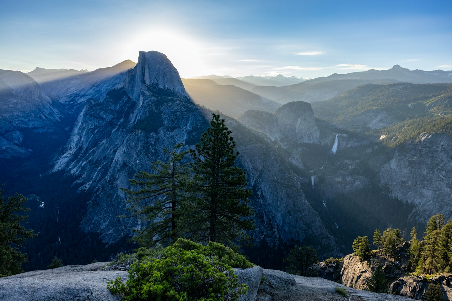 Sunlight peaks over a rugged mountain ridge above forested valleys.