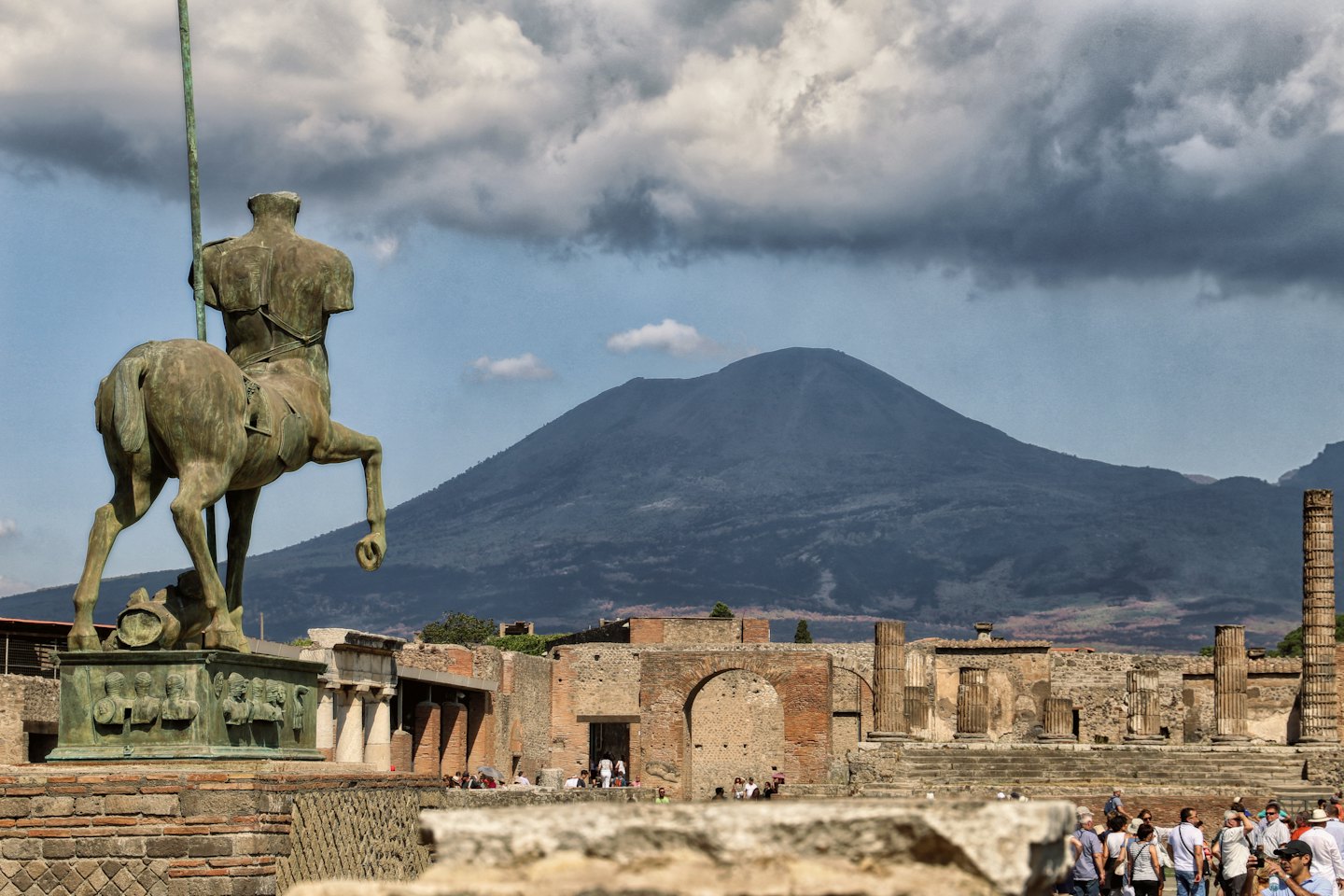 Bronze centaur statue overlooks ancient ruins and a volcano.
